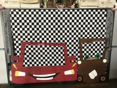 two cardboard cars are on display in front of a checkered wall with other items