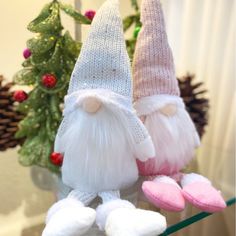 two white and pink gnomes sitting on top of a shelf next to a christmas tree