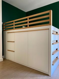 a white bed with wooden slats and shelves underneath it in a green walled room