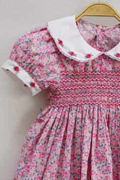 a pink and blue floral dress with collared neckline on a wooden hanger