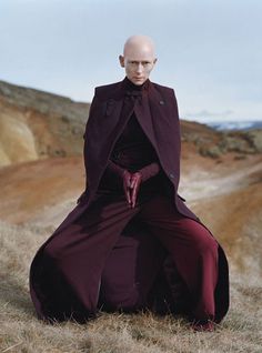 a bald man sitting on top of a grass covered field