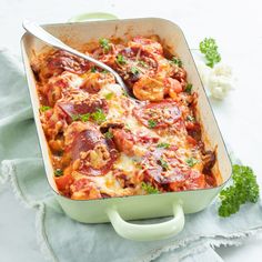 a green casserole dish with meat and sauce in it on a blue towel