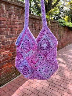 a purple crocheted bag hanging from a brick wall next to a brick sidewalk