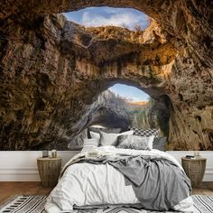 a bed sitting under a cave filled with lots of natural light and rock formations on the wall