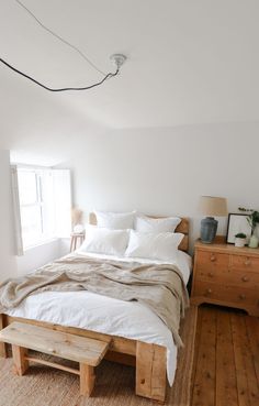 a bed sitting in the middle of a bedroom next to a dresser and window on top of a wooden floor