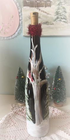 a wine bottle with a tree on it sitting on a table next to christmas trees