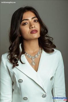 a woman in a white suit and necklace posing for the camera with her hands on her hips