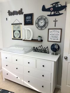 a white dresser topped with lots of drawers next to a wall filled with pictures and clocks