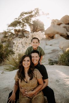 a woman and two boys sitting on top of each other in front of some rocks