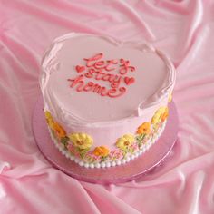 a heart - shaped cake with frosting and flowers on the top sits on a pink cloth