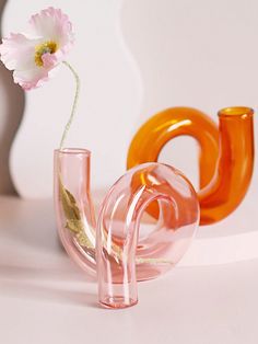 a glass vase with a flower in it next to an orange and pink object on a white surface