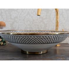 a white bowl sitting on top of a wooden table next to a gold faucet