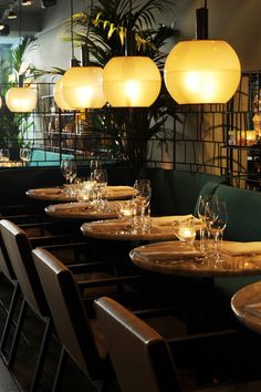 an empty restaurant table with place settings and hanging lights above the dining room tables, which are set for four people