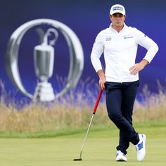 a man standing on top of a green with a golf club in his hand and a trophy behind him