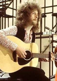 a man with long hair playing an acoustic guitar