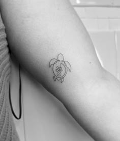 a black and white photo of a small turtle tattoo on the left arm with an omen symbol