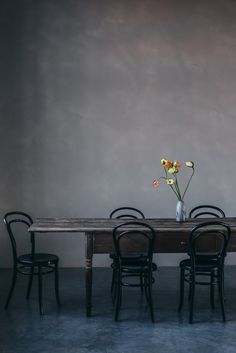 a wooden table with four chairs and a vase filled with yellow flowers on top of it