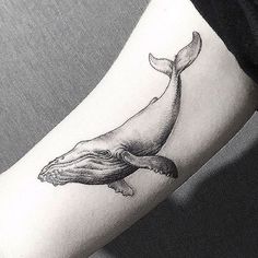 a black and white photo of a woman's arm with a whale tattoo on it