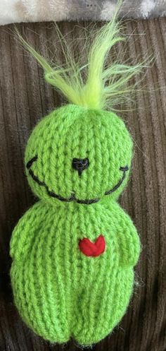 a crocheted green doll with a red heart on it's chest sitting on a couch