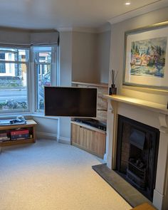 a living room with a fire place, television and window in the corner on the far wall