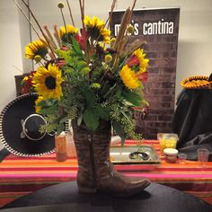 a cowboy boot with sunflowers and other flowers sits on a table in front of a sign