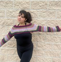 a woman standing in front of a brick wall wearing leggings and a crocheted sweater