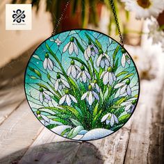 a stained glass window hanging from a chain on a table with flowers in the background