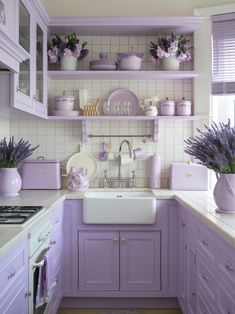 a kitchen with lavender colored cabinets and white counter tops, purple flowers in vases on the shelf