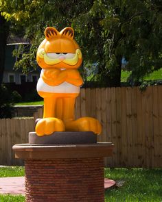 a large yellow cat statue sitting on top of a brick pedestal in front of a fence