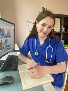 a woman in scrubs sitting at a desk with a notebook and computer on it