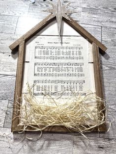 a wooden frame with sheet music in the shape of a house and a cross on top