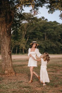 a mother and daughter playing in the grass under a tree with their arms around each other