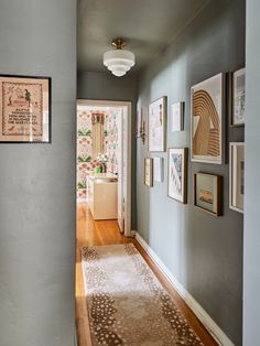 a hallway with pictures on the wall and a rug in front of it, next to a doorway