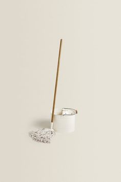 a white cup with a wooden handle and a duster on the floor next to it