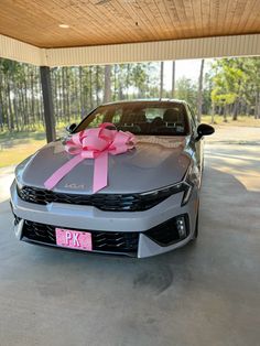 a gray car with a pink bow on it's hood parked in a garage