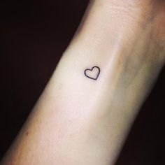 a small heart tattoo on the wrist that is black and white with a tiny outline