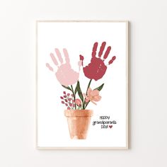 a card with hand prints and flowers in a pot on top of a white wall