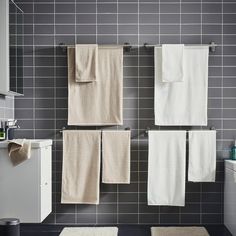 towels hanging on the wall in a bathroom with grey tiles and white cabinets, along with a sink