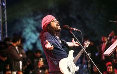 a bearded man singing into a microphone and holding a guitar in front of an audience