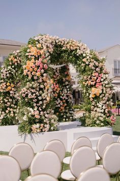 an outdoor ceremony setup with white chairs and pink flowers on the back of the chair