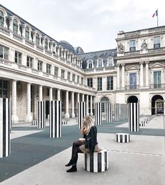 a woman sitting on top of a black and white block in front of a building