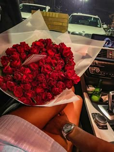 a person sitting in a car holding a bouquet of red roses on the dash board