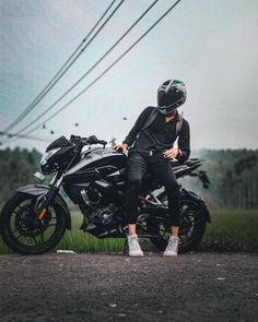 a man sitting on top of a black motorcycle in the middle of a road next to power lines