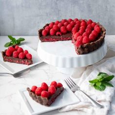 a chocolate tart topped with raspberries on top of a white cake plate