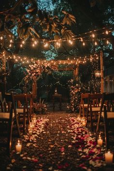 an outdoor ceremony with candles and flowers on the aisle, surrounded by greenery and string lights