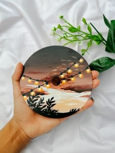 a hand holding a disc with string lights on it next to a green leafy plant