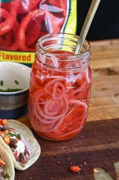 two tacos sitting on top of a cutting board next to a jar of pickled onions