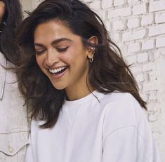 a woman smiling and looking at her cell phone while standing next to a brick wall