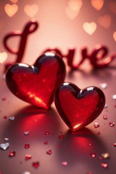 two shiny red hearts sitting next to each other on top of a pink surface with lights in the background