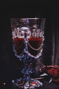 two wine glasses with red liquid in them on a black surface next to a rose